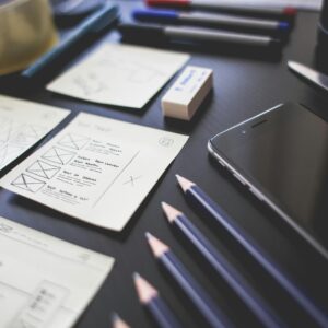 A creative workspace featuring UI design plans, pencils, a smartphone, and other office tools.