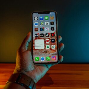 A hand holding a smartphone displaying app icons, with a modern minimalistic background.